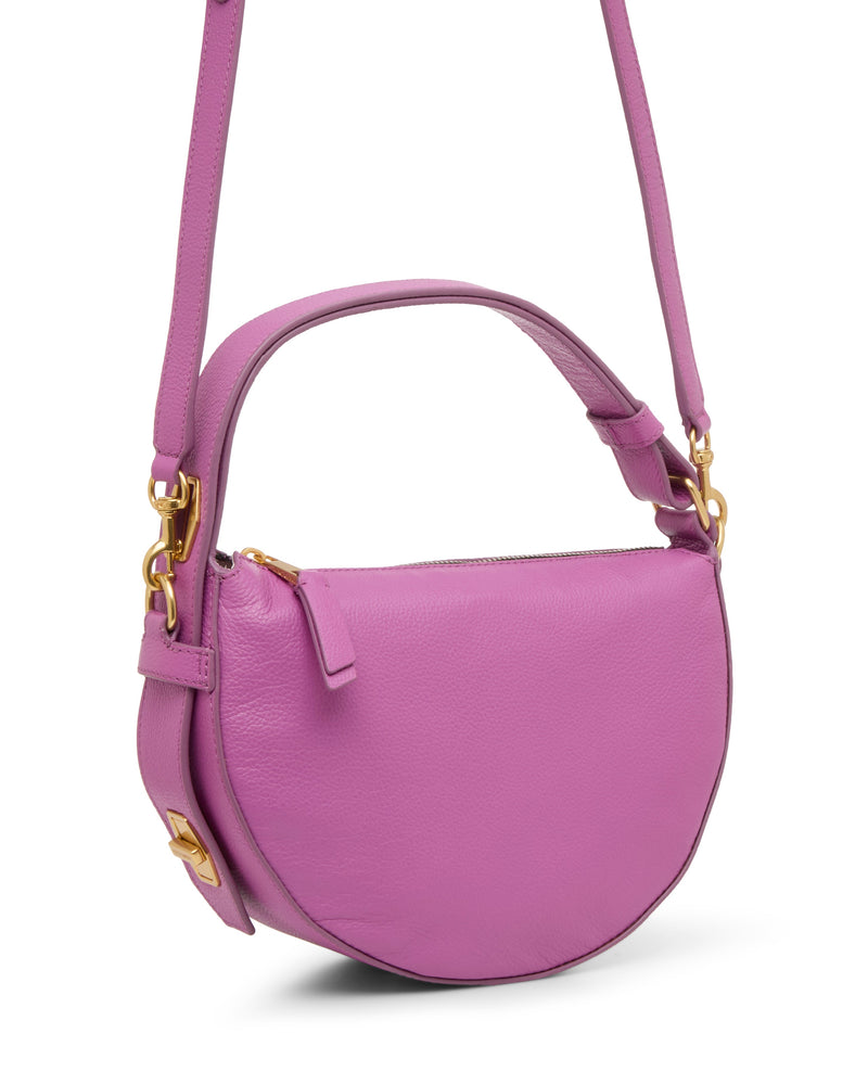 The Vince Camuto Karla Crossbody Bag is a stylish round light purple leather handbag with a half-moon shape, short handle, long adjustable shoulder strap, gold-tone hardware, and a zippered top closure.