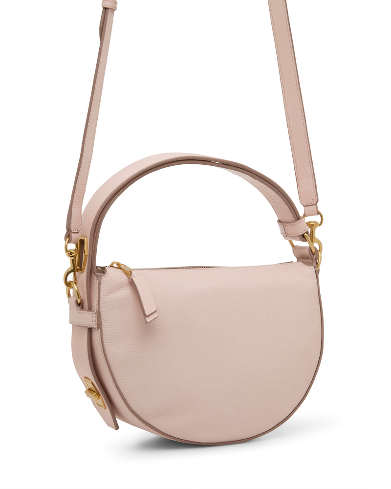 The Vince Camuto Karla Crossbody Bag features light pink leather, a rounded shape, gold-tone hardware, top handle, adjustable shoulder strap, zippered closure, and a sleek minimalist design.