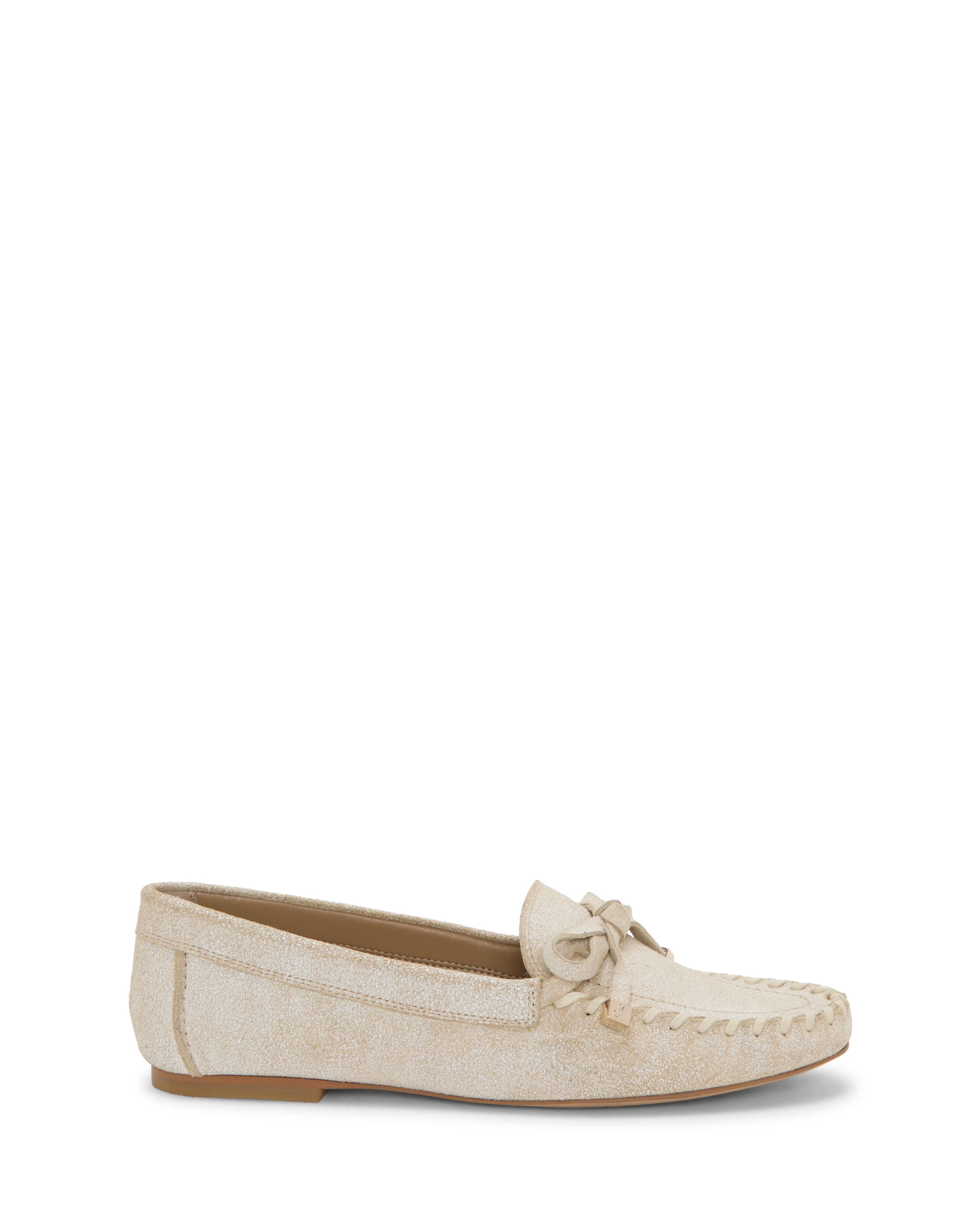 The Katena Flat Loafer by Vince Camuto is a beige suede shoe with a moc-inspired silhouette, decorative bow, and stitching on the upper, displayed in side view against a white background.