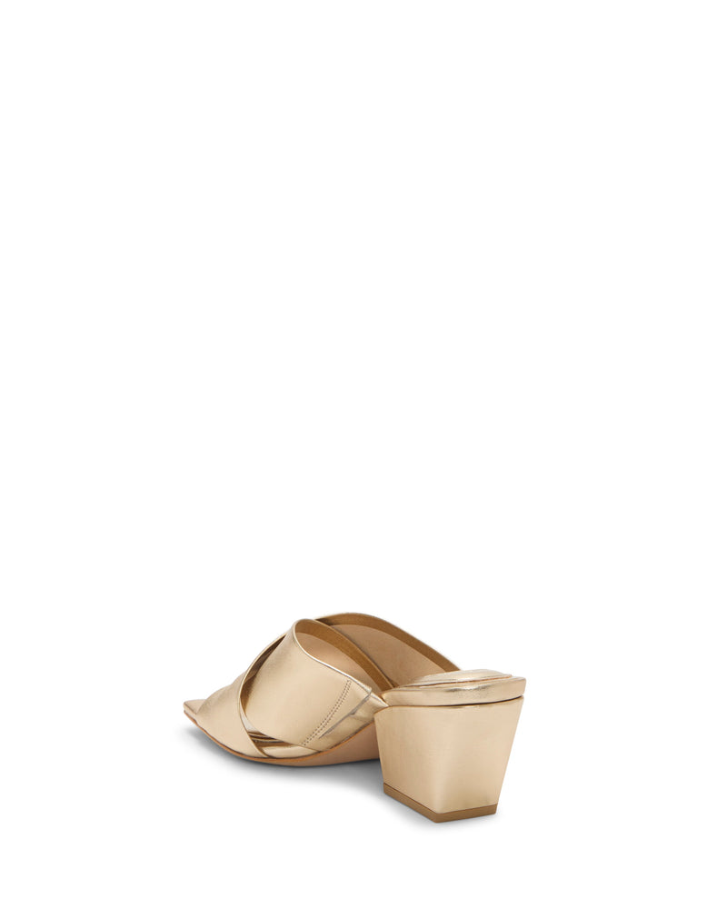 The Vince Camuto Kespa Mule is a gold, open-toe block heel sandal featuring a crisscross upper, shown from the back and slightly to the side against a plain white background.