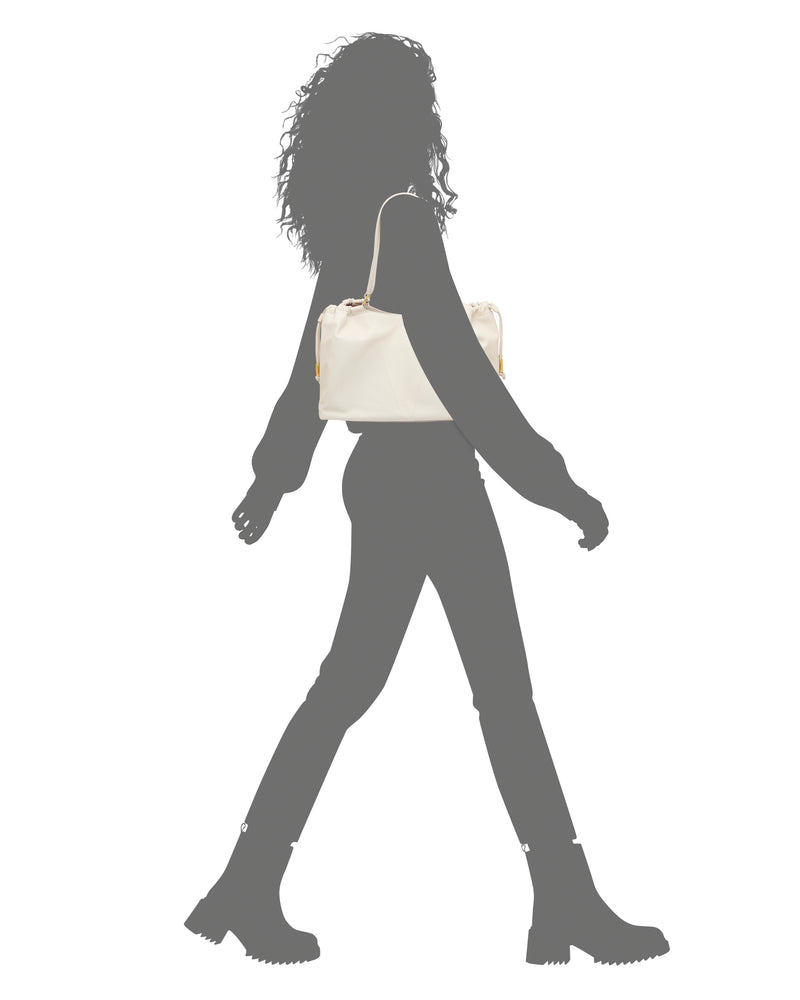 A silhouette in grayscale walks wearing boots, carrying the Vince Camuto Leane Tote Bag in color on their shoulder—it's the only colorful feature in the image.