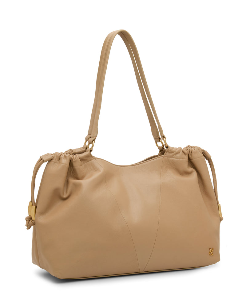 The Vince Camuto Leane Tote Bag is a beige leather shoulder bag with gold hardware, double handles, side drawstring details, and a small gold logo at the bottom right corner.