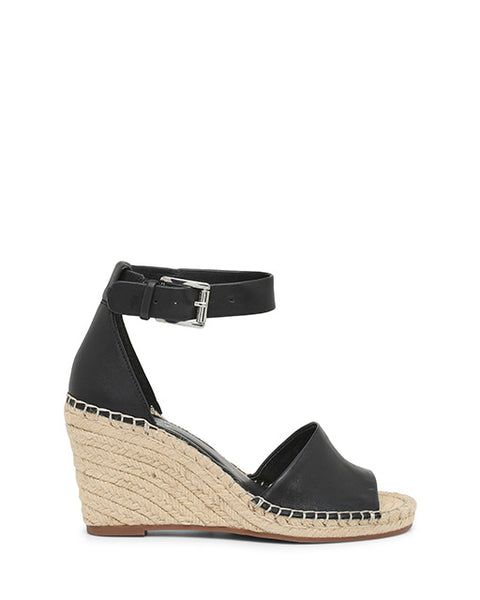 The Leera Espadrille Wedge Sandal by Vince Camuto is a black open-toe wedge with an ankle strap and buckle, featuring a natural woven espadrille heel and white stitching along the edges.
