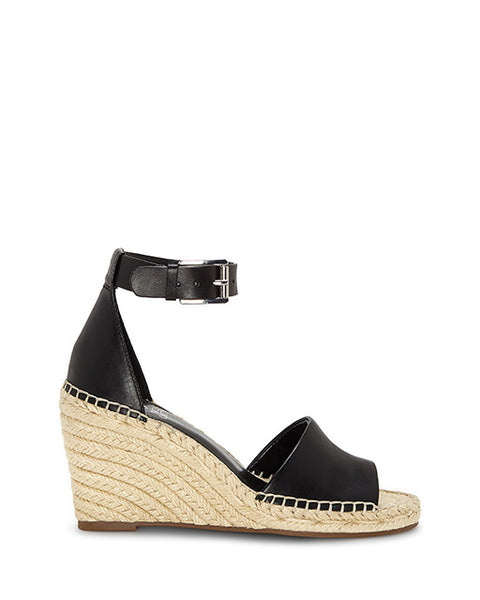 The Leera Espadrille Wedge Sandal by Vince Camuto is a black wedge sandal featuring an open toe, ankle strap with buckle, and a woven straw platform heel. The front and heel areas are closed, with visible stitching along the edges.