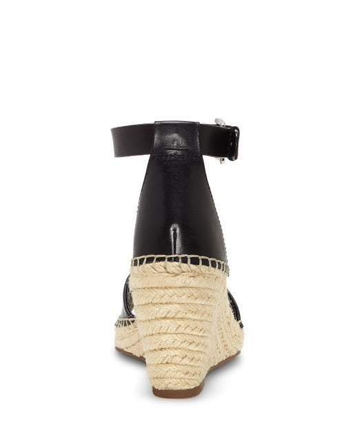 Rear view of the Vince Camuto Leera Espadrille Wedge Sandal in black, showcasing an ankle strap with buckle, a closed back, and a braided jute platform wedge heel.