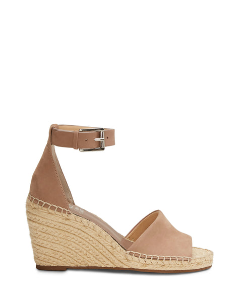 The Leera Espadrille Wedge Sandal by Vince Camuto features a beige design with an open toe, ankle strap, and silver buckle. Its wedge heel is wrapped in braided rope for a classic espadrille look. The sandal is shown against a plain white background.