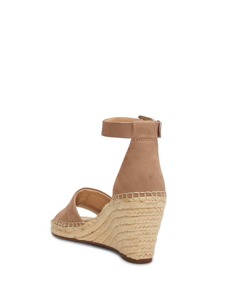 From behind and slightly to the side, the Vince Camuto Leera Espadrille Wedge Sandal is shown in beige, featuring a closed back, ankle strap, and a woven espadrille-style platform heel.