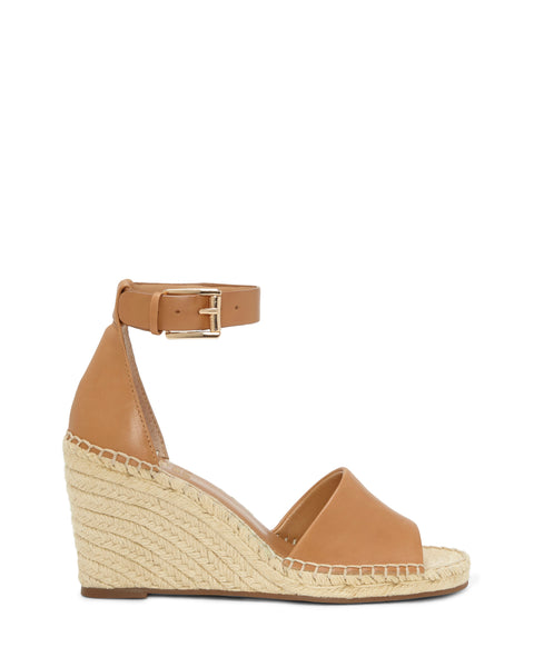 The Leera Espadrille Wedge Sandal by Vince Camuto features tan leather with an open toe, ankle strap, and buckle. Its wedge heel is wrapped in braided jute for a classic espadrille style. Shown against a plain white background.