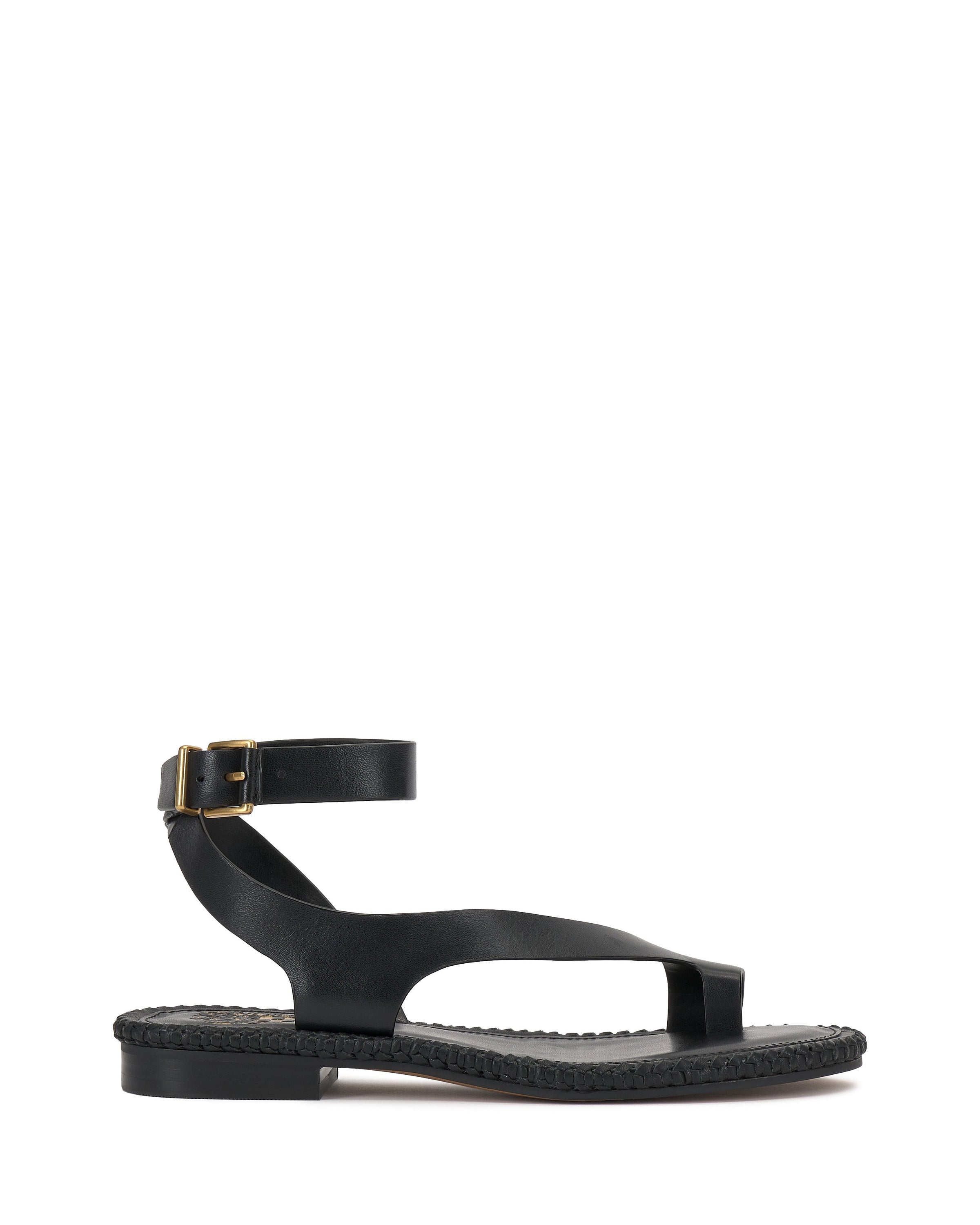 The Vince Camuto Libahs Sandal is a black flat sandal with an asymmetrical design, thick ankle strap with gold buckle, wide toe strap, and braided sole detail. It’s shown against a plain white background.