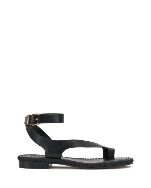 The Vince Camuto Libahs Sandal is a black flat sandal with an asymmetrical design, thick ankle strap with gold buckle, wide toe strap, and braided sole detail. It’s shown against a plain white background.