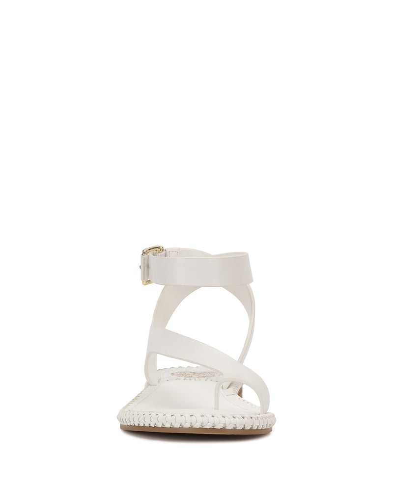 The Vince Camuto Libahs Sandal features a modern flat design in white with crisscross straps, an adjustable ankle strap, and braided trim around the sole, shown from the front against a plain white background.
