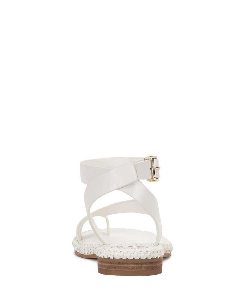 The Libahs Sandal by Vince Camuto is a modern flat sandal with crisscross straps, an adjustable ankle strap with a gold buckle, woven sole detailing, and a flat brown heel.