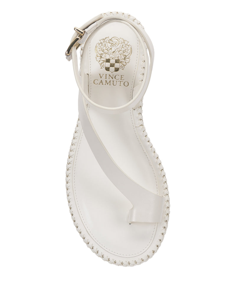 The Vince Camuto Libahs Sandal is a modern white flat featuring a single toe strap, diagonal instep strap, and adjustable ankle strap. The insole showcases gold Vince Camuto branding with a decorative emblem near the heel.