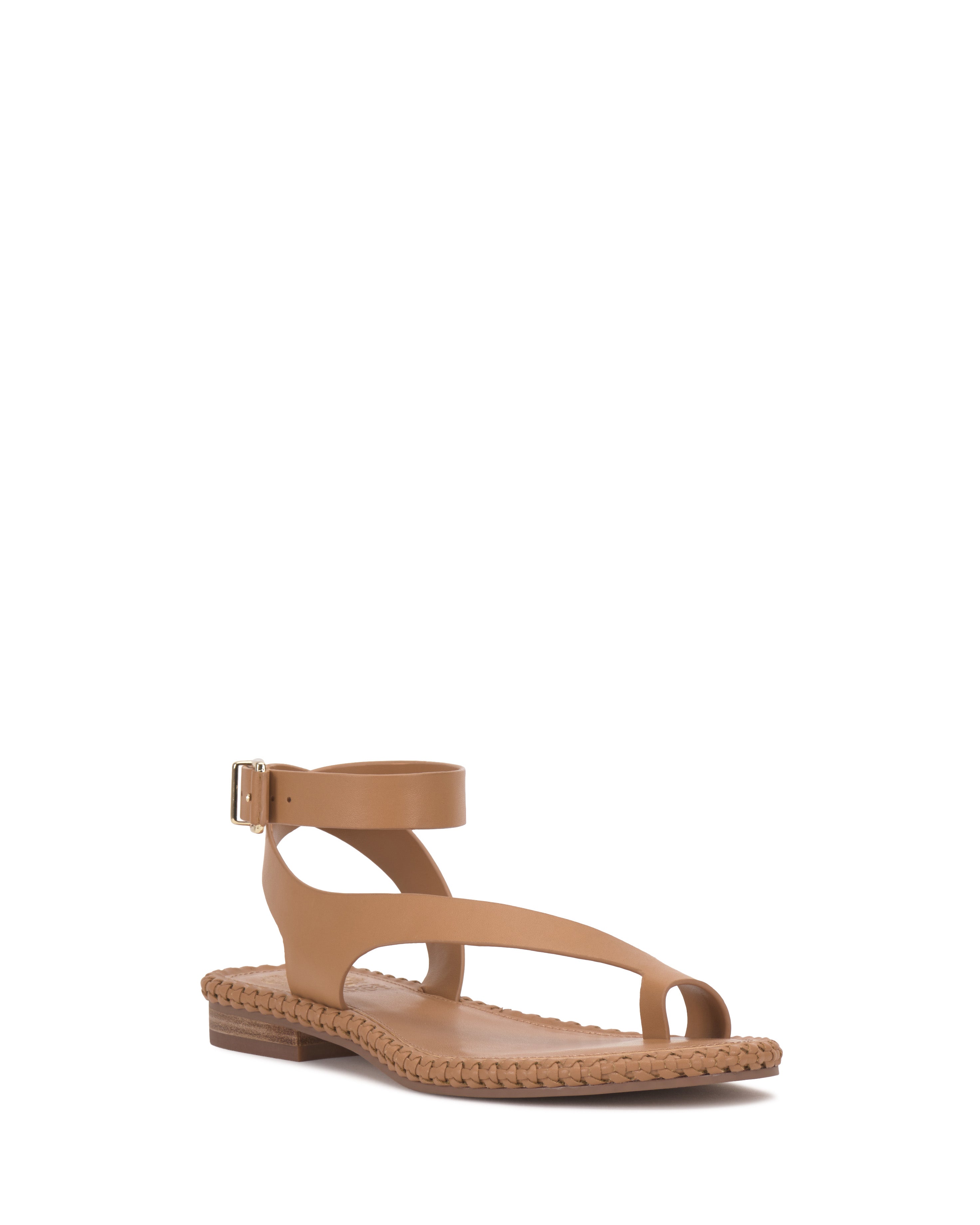 The Vince Camuto Libahs Sandal is a tan modern flat with a toe loop, adjustable ankle strap with buckle, woven sole detailing, and low wooden heel, featuring a minimalist design. Shown on a plain white background.