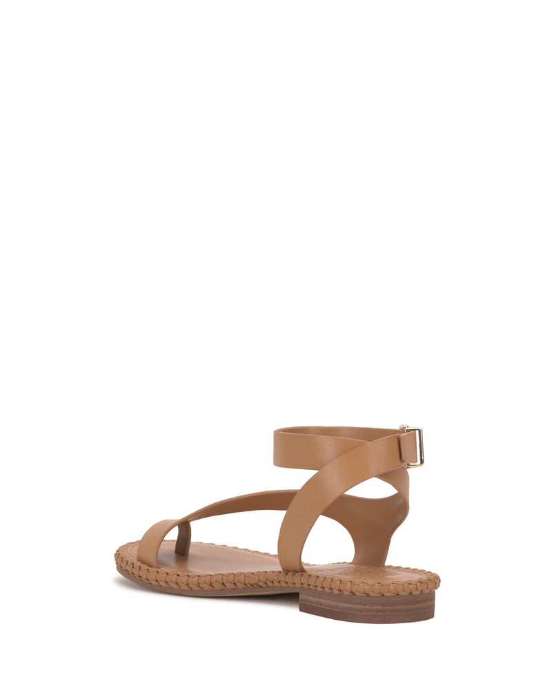 The Vince Camuto Libahs Sandal is a tan modern flat with a woven sole, open toe, and crisscross adjustable ankle strap with a small buckle, shown from the rear against a white background.