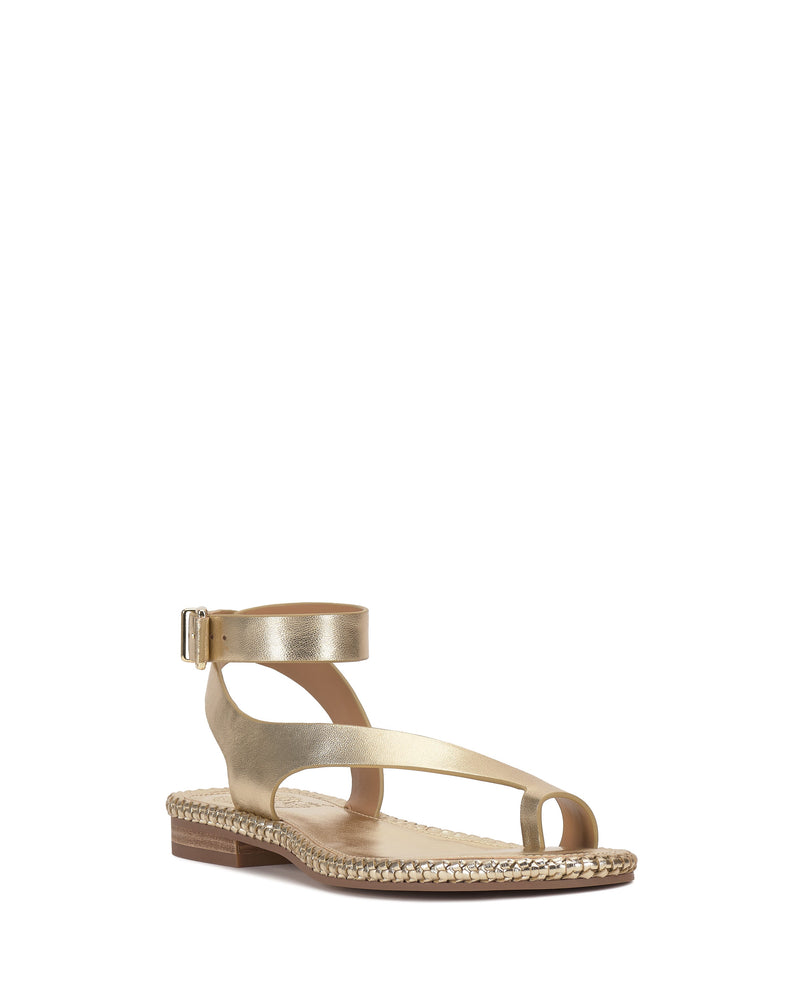 The Libahs Sandal by Vince Camuto is a modern gold flat with an adjustable ankle strap, side buckle, open toe, and braided edging on the sole, shown against a white background.
