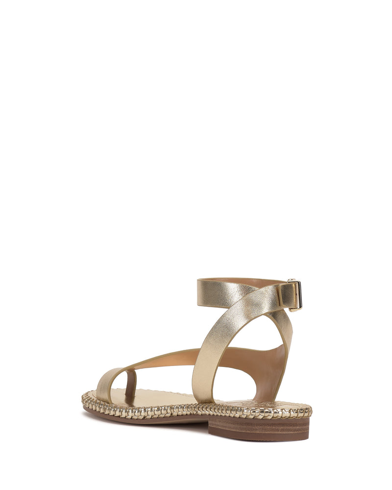 The Libahs Sandal by Vince Camuto is a modern flat in metallic gold with an adjustable ankle strap, buckle, open toe, low heel, and braided sole detail, shown against a white background.