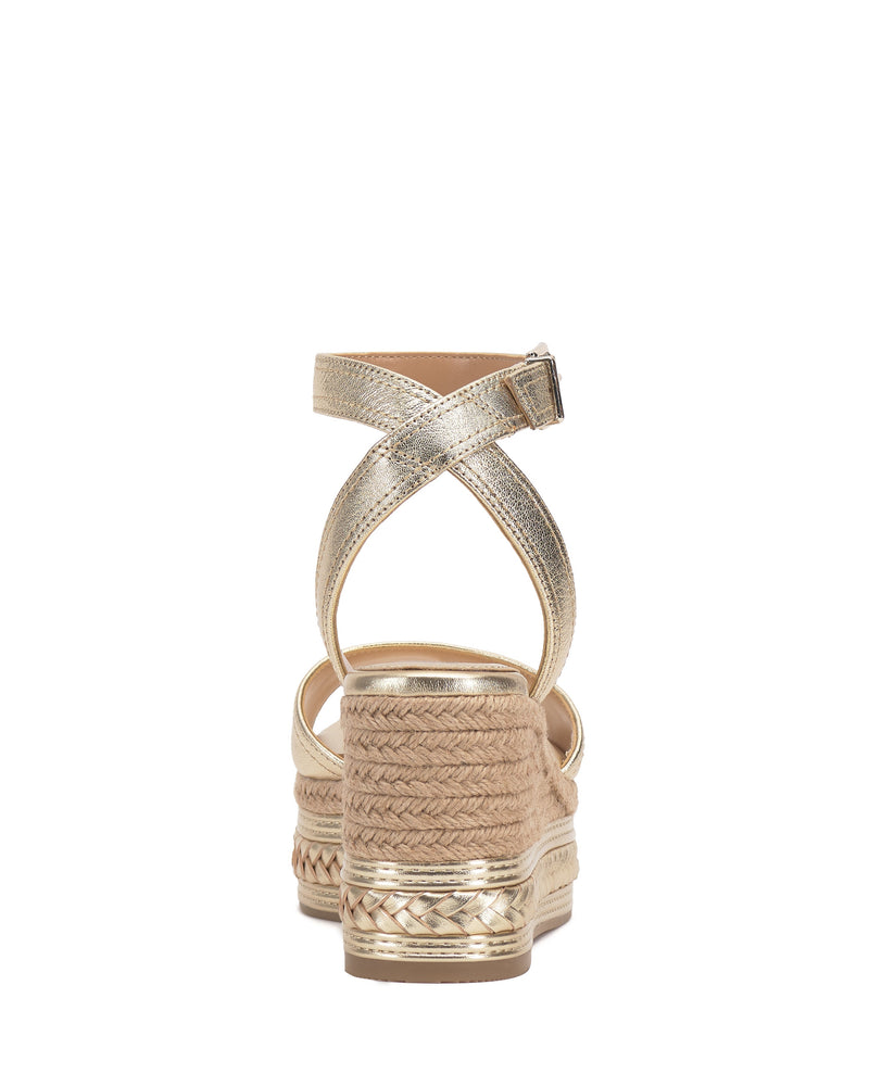 The Vince Camuto Lilla Espadrille Wedge Sandal features gold metallic leather, a braided jute wedge, woven sole pattern, and back view of a crisscross ankle strap with buckle.