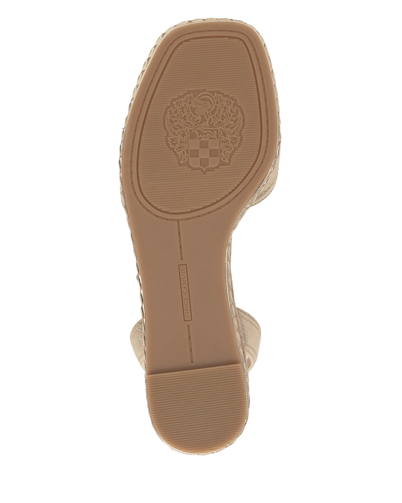 The image shows the sole of the Vince Camuto Lilla Espadrille Wedge Sandal, made from beige leather. The sole has textured lines for grip and an embossed crest with a shield and decorative details near the center.