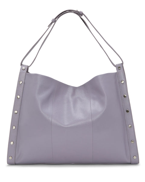 The Vince Camuto Lisha Tote Bag is a spacious, soft-sided lavender leather tote featuring silver studs and a wide shoulder strap—a stylish and modern carryall.