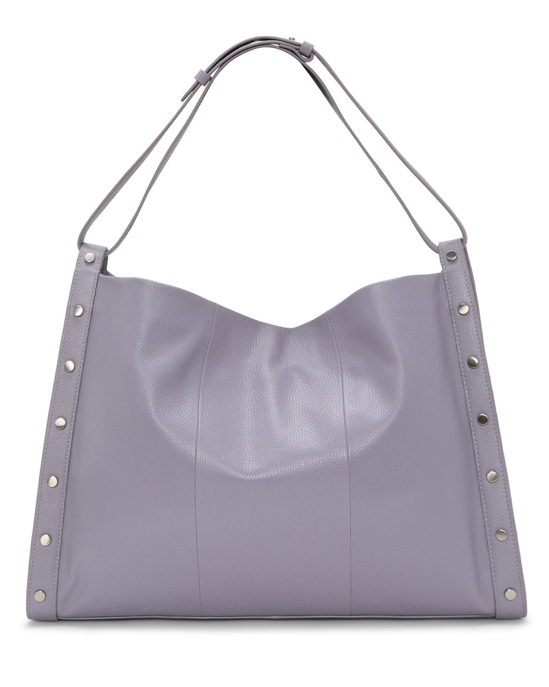 The Vince Camuto Lisha Tote Bag is a spacious, soft-sided lavender leather tote featuring silver studs and a wide shoulder strap—a stylish and modern carryall.