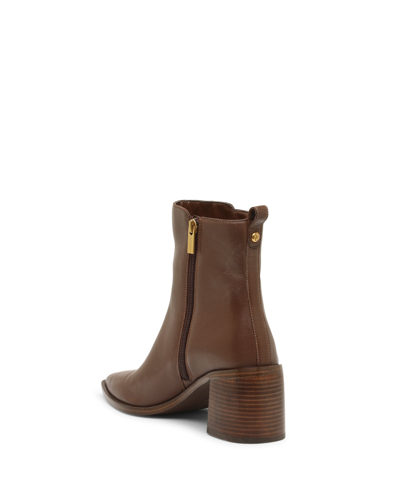 The Lorelai Bootie by Vince Camuto features a brown pointed toe, medium stacked wooden block heel, side zipper with a gold pull, and a back pull tab. This modern style boot is photographed from a rear side angle against a white background.