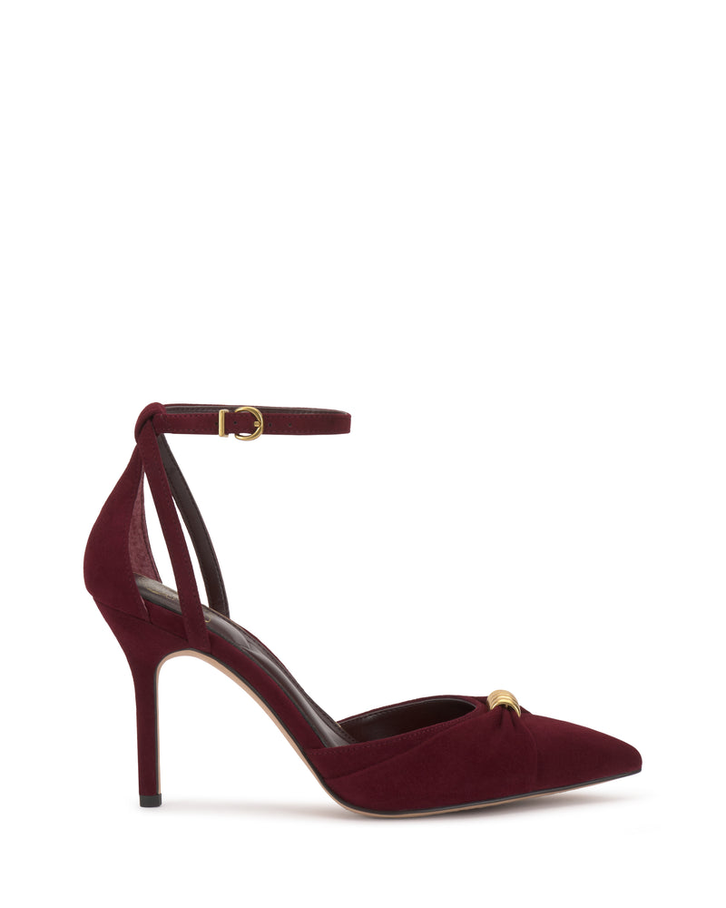 The Vince Camuto Mallie Pump is a burgundy suede high heel featuring a pointed toe, ankle strap with gold buckle, and a small gold embellishment on the front.