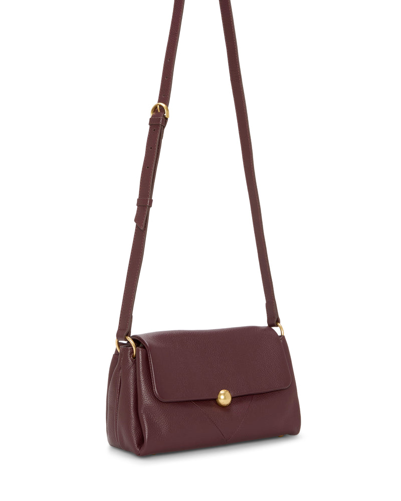 The Vince Camuto Medna Crossbody Bag features burgundy leather, a long adjustable strap, gold hardware, and a flap closure with a gold button. Its structured rectangular shape adds timeless style to any outfit.