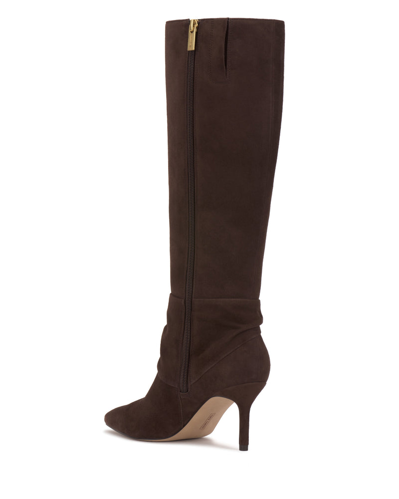The Meezo Knee High Boot by Vince Camuto features dark brown suede, a pointed toe, skinny heel, inner side zipper with a chic gold pull tab, and a slightly slouchy ankle design for added style.