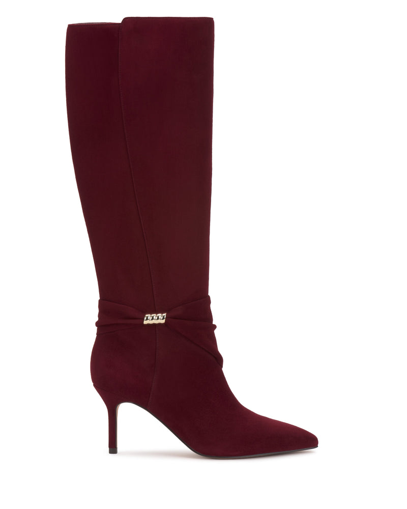 The Meezo Knee High Boot by Vince Camuto is a single knee-high boot in deep burgundy suede, featuring a pointed toe, skinny heel, and a gold chain hardware accent detail near the ankle.