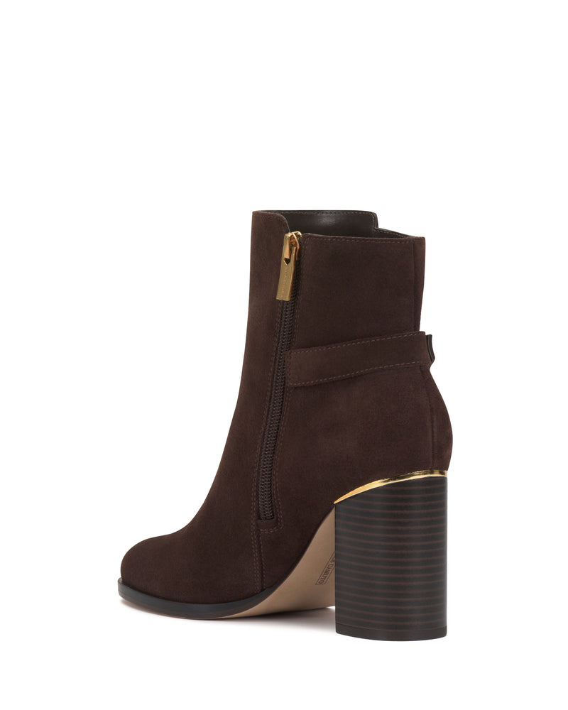 The Melvani Bootie by Vince Camuto is a dark brown suede ankle boot featuring a chunky high heel with a ribbed texture, gold zipper, gold trim near the heel, and a strap detail around the back. The sole is beige.