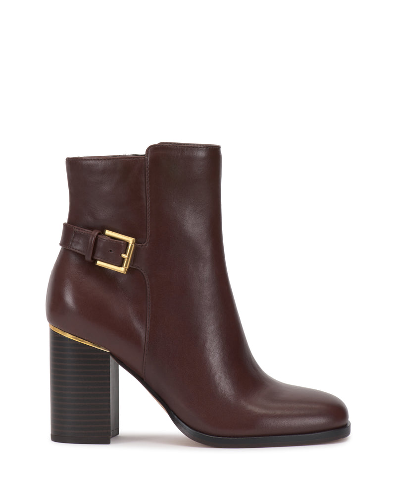 The Melvani Bootie by Vince Camuto is a dark brown leather ankle boot featuring a block heel, gold buckle detail, and rounded toe, showcased in a side profile against a white background.