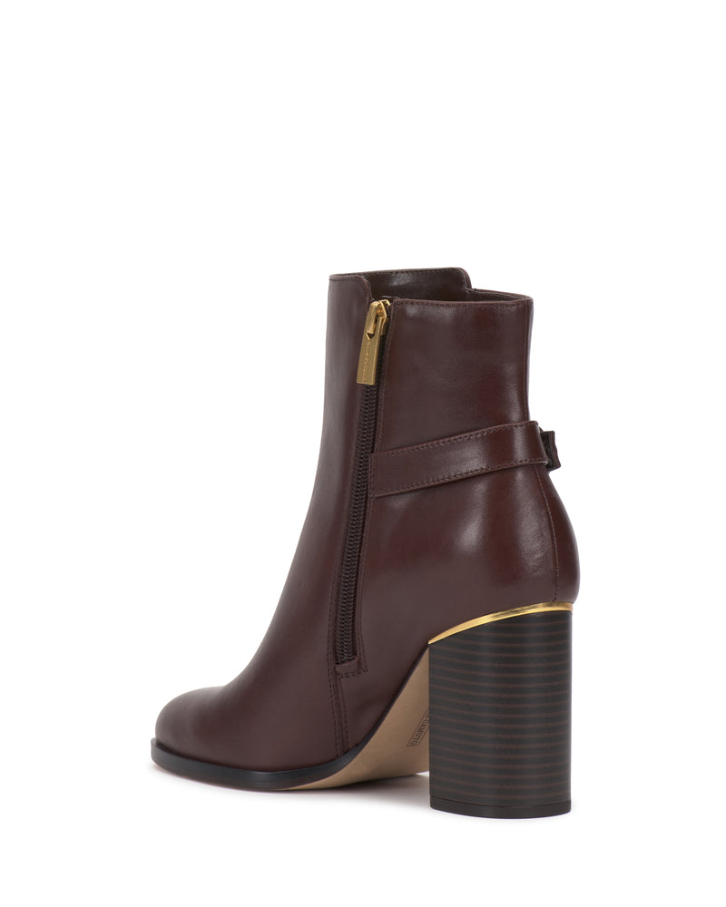 The Melvani Bootie by Vince Camuto is a brown leather ankle boot featuring a chunky stacked heel, gold side zipper, and decorative strap detail at the back, photographed on a white background.