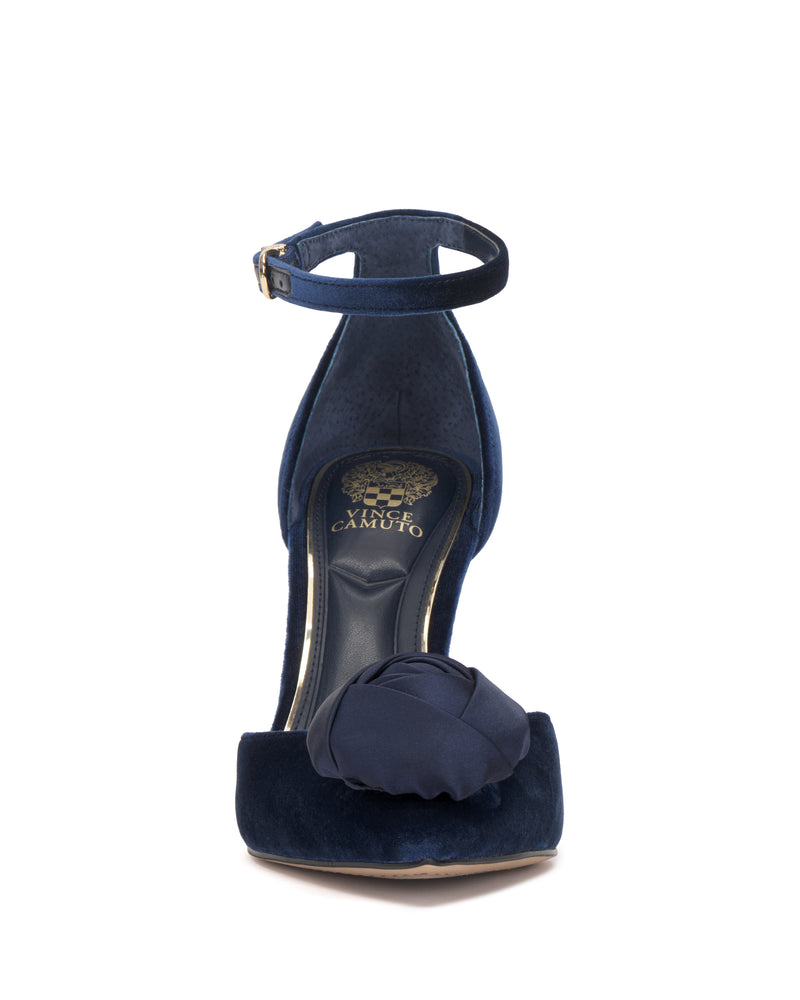 The Mirezzo Pump by Vince Camuto is a navy blue velvet stiletto with an ankle strap and a bow on the toe, seen from the front. The insole is black with gold Vince Camuto branding.