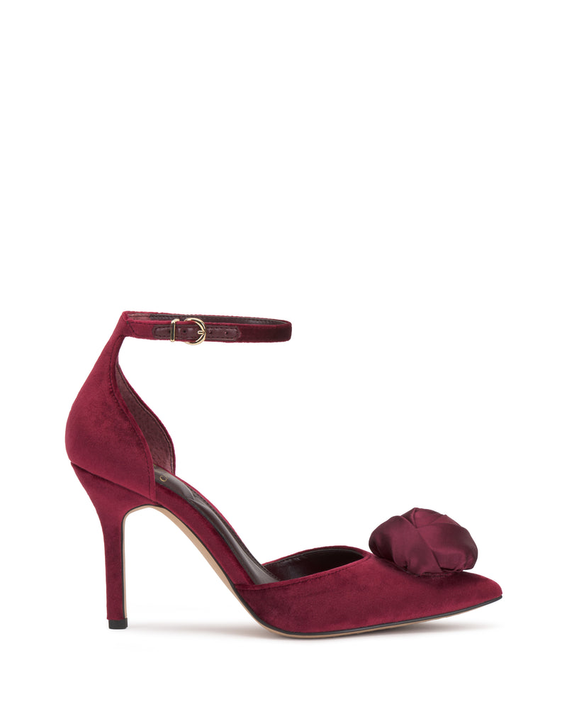 The Vince Camuto Mirezzo Pump is a burgundy stiletto with an ankle strap, pointed toe, and a fabric flower on the toe, shown on a white background.