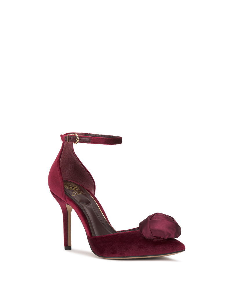 The Mirezzo Pump by Vince Camuto features a stiletto heel, ankle strap, and a large satin bow on the pointed toe in burgundy, displayed against a white background.