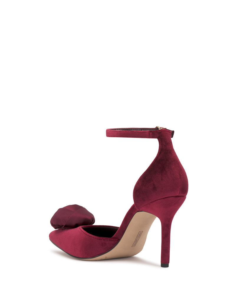 The Vince Camuto Mirezzo Pump is a burgundy stiletto with an ankle strap, pointed toe, and a bold fabric bow on the front, combining elegance with modern style.