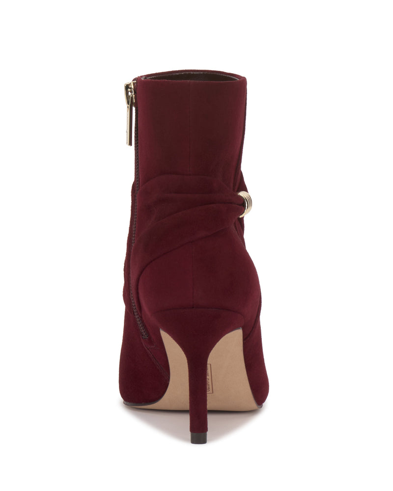 The Vince Camuto Murlea Bootie is shown from the back in burgundy suede, featuring a skinny heel, decorative wrap detail with a metal accent, and a visible side zipper.
