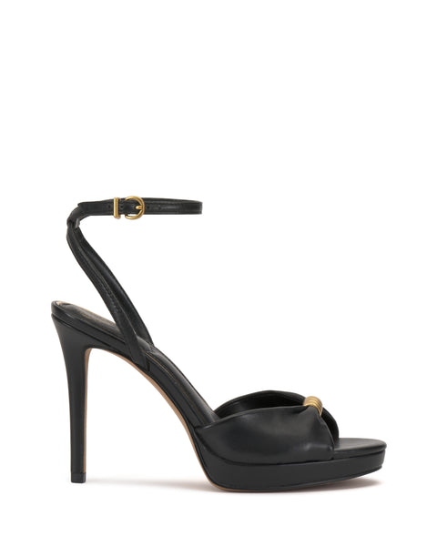 The Vince Camuto Neala Sandal is a black high-heeled sandal with an ankle strap, gold buckle, and small gold accent on the toe strap, shown on a white background.
