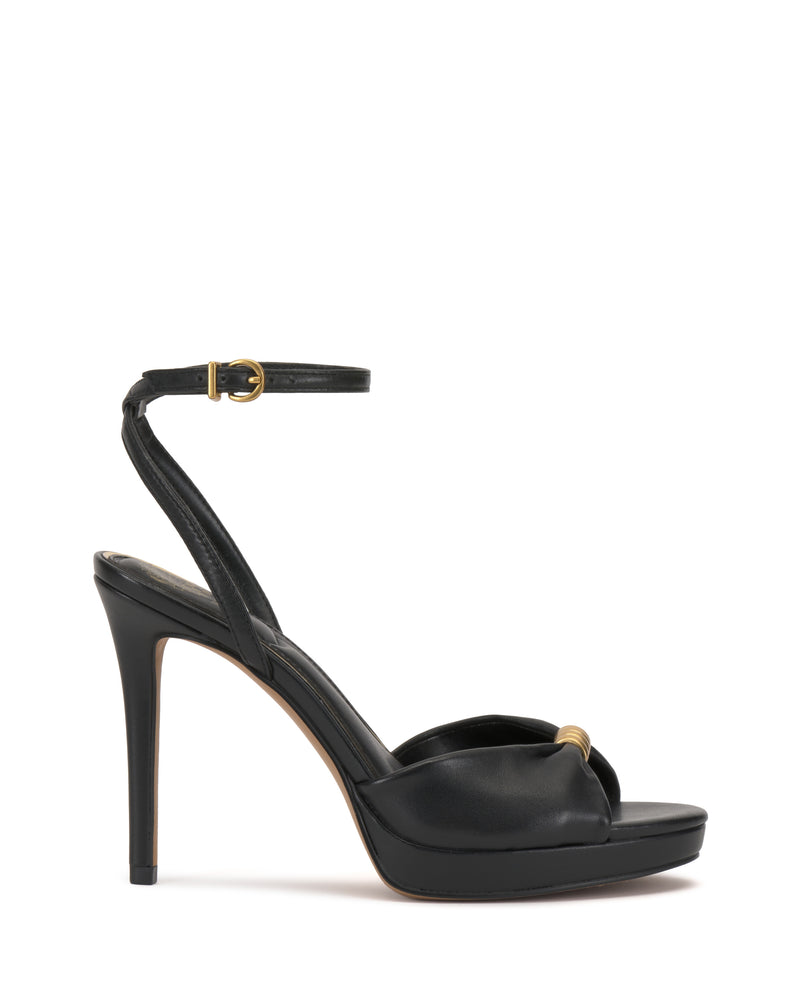 The Vince Camuto Neala Sandal is a black high-heeled sandal with an ankle strap, gold buckle, and small gold accent on the toe strap, shown on a white background.