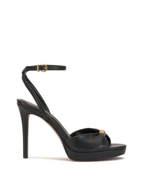 The Vince Camuto Neala Sandal is a black high-heeled shoe with a skinny ankle strap and gold buckle, peep toe, gold accent on the front strap, slim tall heel, and a slight platform for an elegant touch.