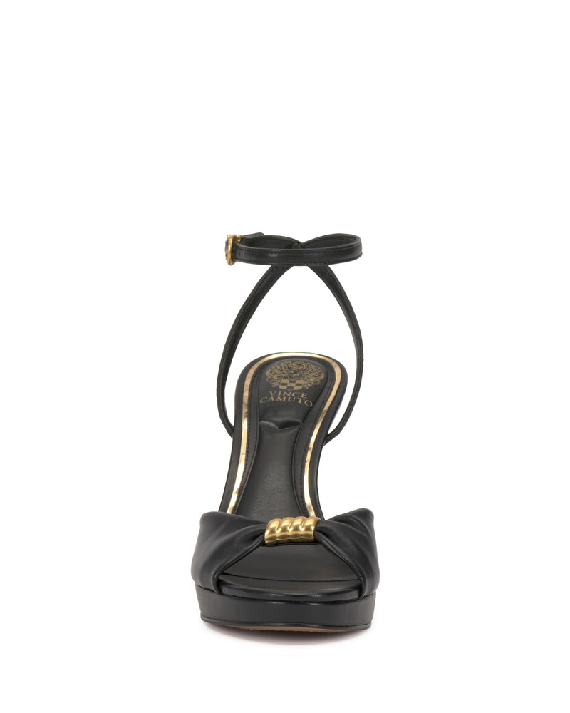 The Neala Sandal by Vince Camuto is a black high-heeled sandal featuring an ankle strap, gold buckle, and gold chain detail on the front, shown from the front against a white background.