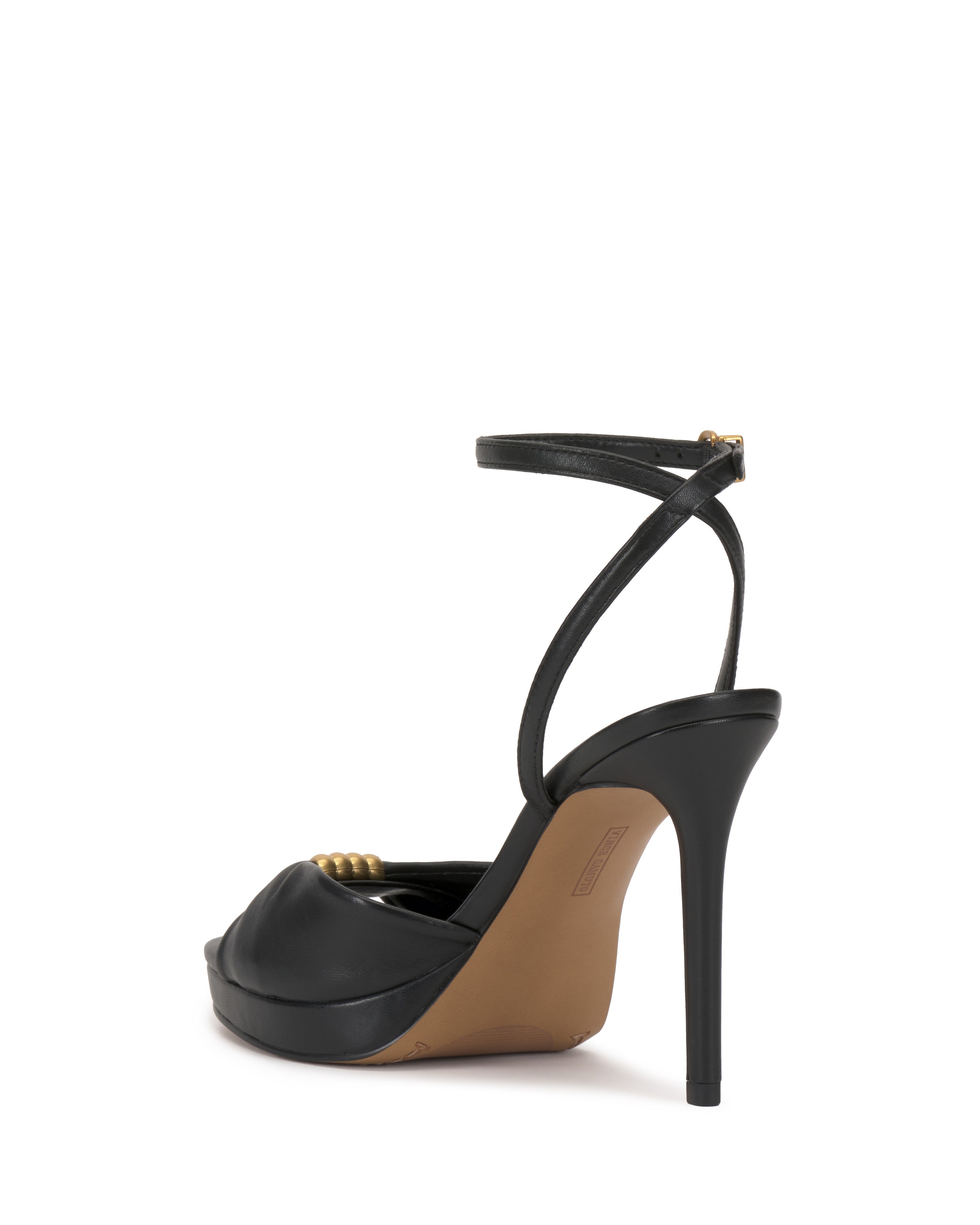 The Vince Camuto Neala Sandal is a black high-heeled sandal with an ankle strap and peep-toe design, shown from the rear. It features a tan sole and a tall, thin heel.