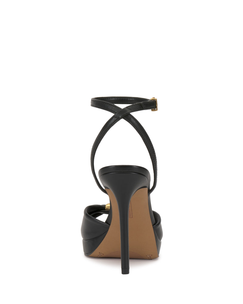The Vince Camuto Neala Sandal is a black high-heeled shoe with a thin, crisscross ankle strap and buckle, a slender stiletto heel, and a tan sole—shown here from the back.