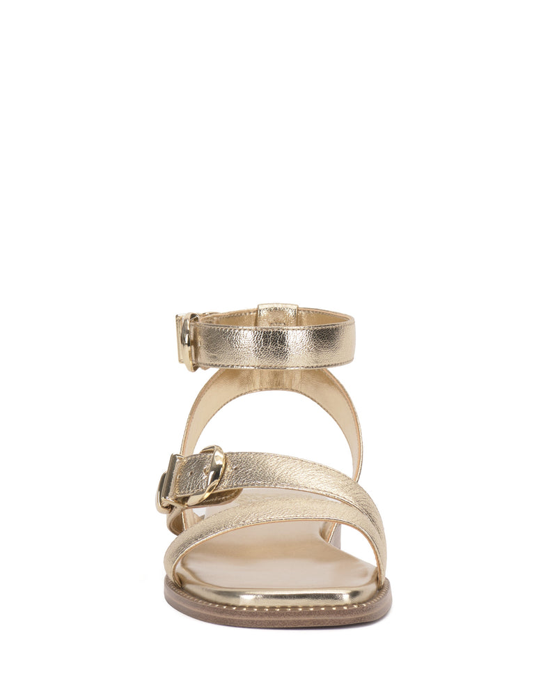 The Vince Camuto Neiko Sandal features a metallic gold finish, two buckled straps, and a flat sole with detailed stitching visible around the edge.