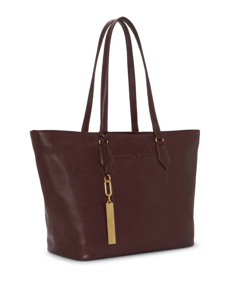The Vince Camuto Noemi Tote Bag is a spacious burgundy leather tote with double handles, gold hardware, and a rectangular gold tag. Its simple, structured design and minimal detailing create an effortlessly chic look.