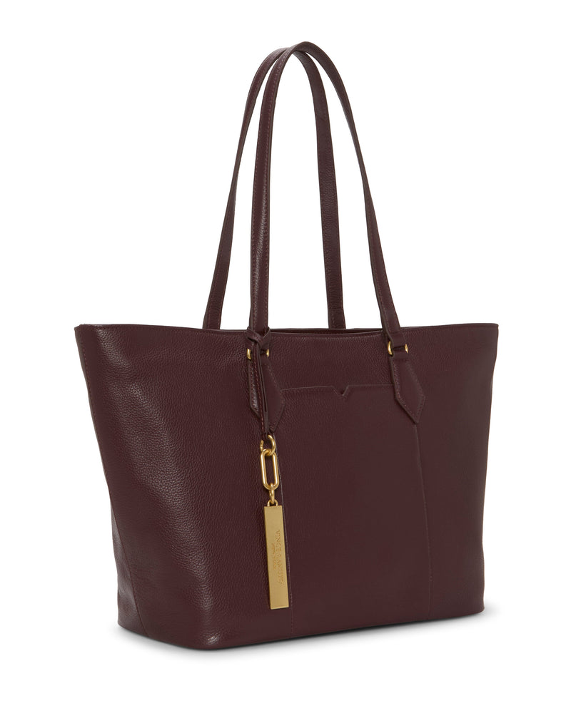 The Vince Camuto Noemi Tote Bag is a spacious dark burgundy leather tote with double handles, gold-tone hardware, and a rectangular hanging tag. Its elegant design and textured finish make it perfect for work.