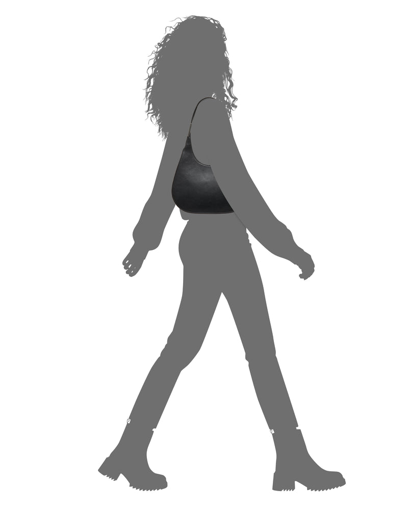 Silhouette of a person walking, wearing boots, pants, a long-sleeve top, and carrying the Vince Camuto Noli Hobo Bag. Their hair is curly and loose.