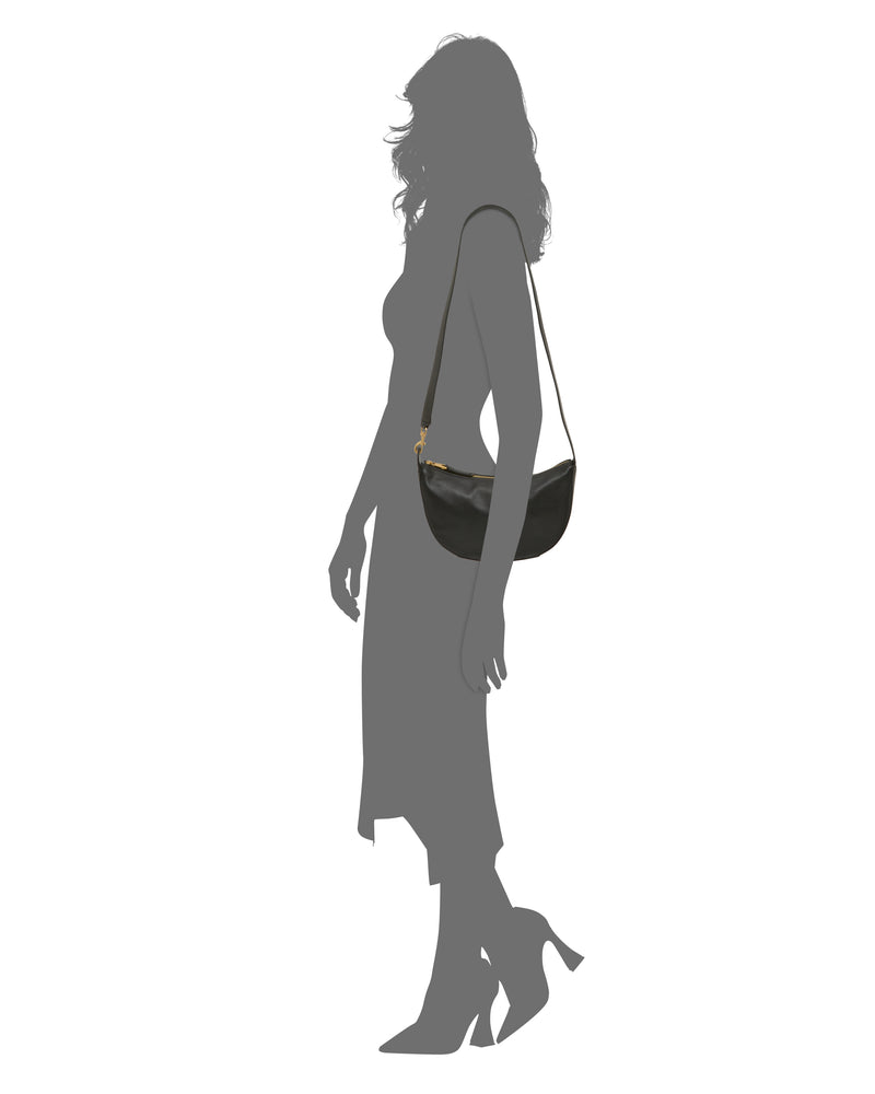 Silhouette of a woman in a mid-length dress and heels, carrying the Vince Camuto Orlie Crossbody Bag—a sophisticated accessory featuring a gold clasp. The background is white.