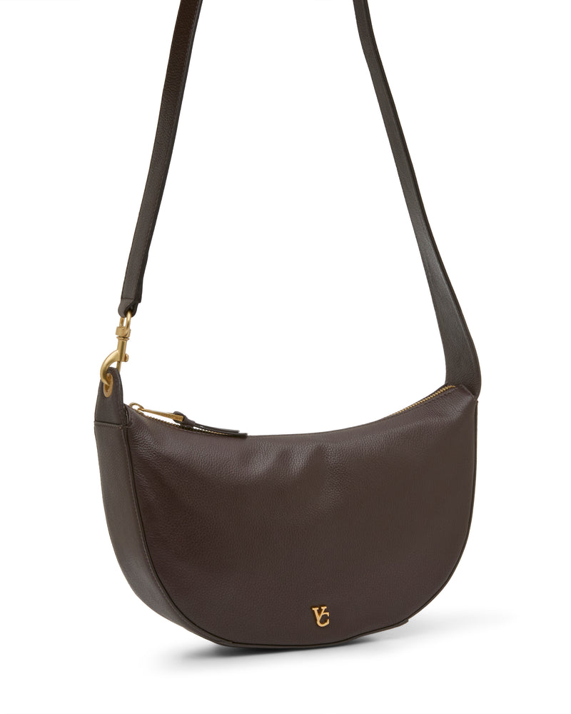The Vince Camuto Orlie Crossbody Bag in dark brown leather features a gold zipper and a small gold logo on the front, shown against a white background, making it an elegant choice for a women’s handbag.